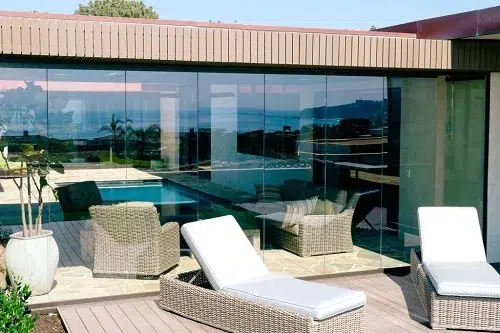 Enclosed frameless sliding glass doors with lounge chairs in front.