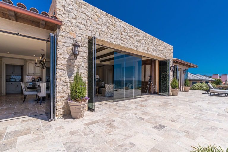 Looking from stone floor patio into open concept living and dining room with frameless sliding glass doors stacked on sides with few panels left stranded in the middle.