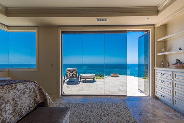 Looking at bedroom with stone flooring and shelving with enclosed frameless glass doors with one frame opened to the patio with an unobstructed view of the patio and ocean.