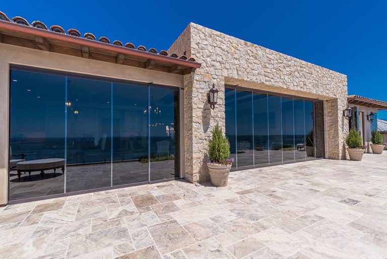 Looking at home from backyard with stone flooring and sliding glass doors enclosed.