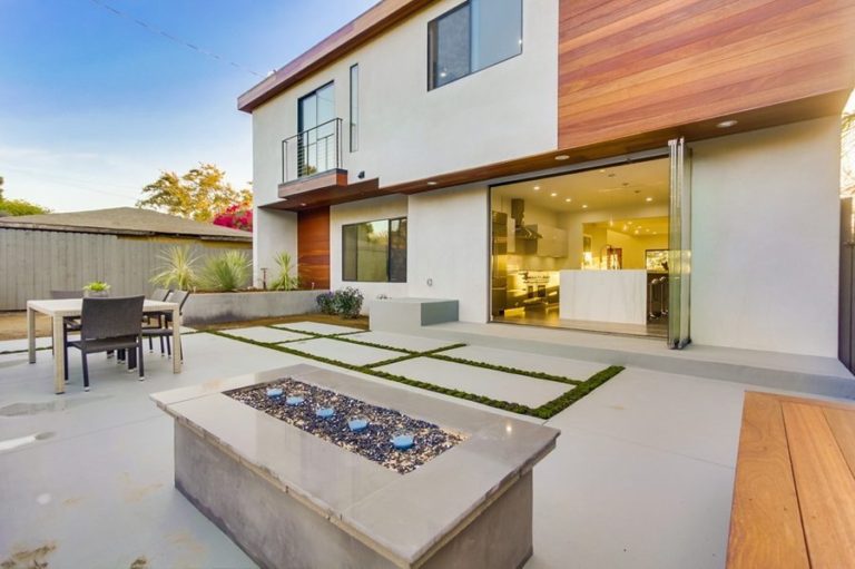 Patio with fireplace and table looking into kitchen with stacked frameless sliding glass doors.