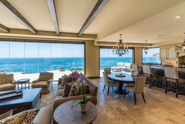 Looking at open concept living, kitchen and dining room with stone floor and frameless sliding glass doors enclosed allowing for unobstructed views of the ocean.