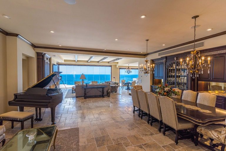 Looking at open concept living and dining room with stone floor and frameless sliding glass doors enclosed allowing for unobstructed views of the ocean.