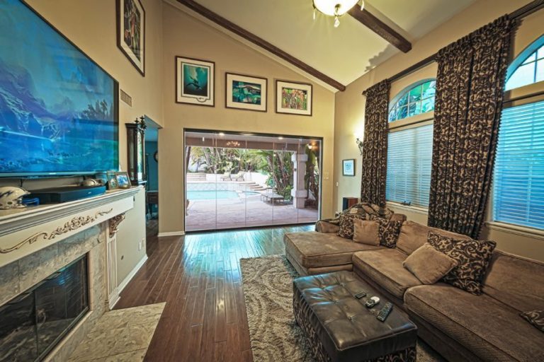 Frameless sliding glass doors connecting living area with tv and fire place with outdoor patio and swimming pool.