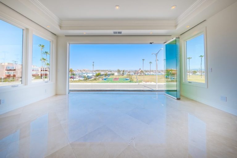 Looking from empty living room into bay with stacked frameless sliding glass doors.