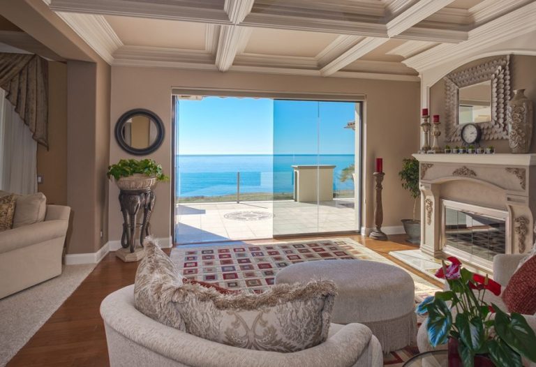 Living room with view of ocean and half enclosed frameless sliding glass doors.