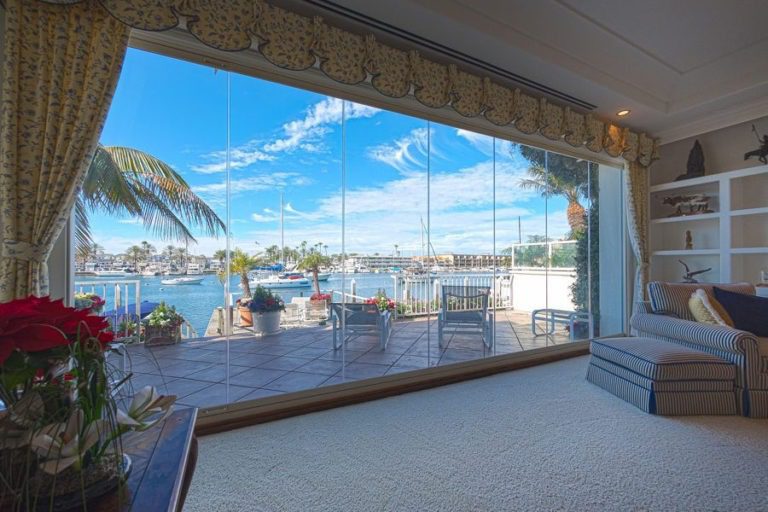 Living room with grey carpet and frameless sliding glass doors overlooking the outdoor patio and bay.