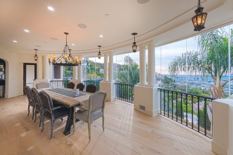 Enclosed frameless sliding glass door dining room patio with natural light and view of hill.