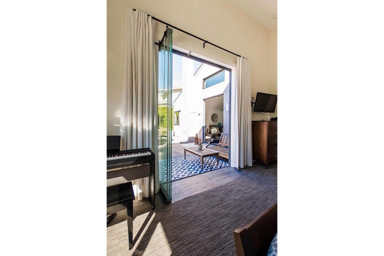 Bedroom with piano in the corner and stacked frameless sliding glass doors showing the outdoors.