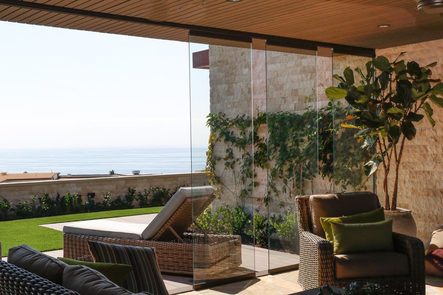 Partially open sliding glass doors connecting indoor patio with yard overlooking the ocean.
