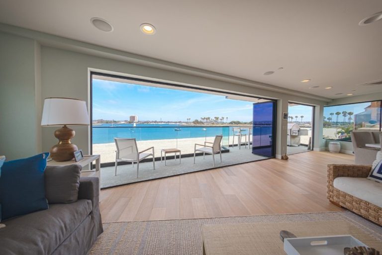 Looking from living and dining room out to patio with opened frameless sliding glass doors.