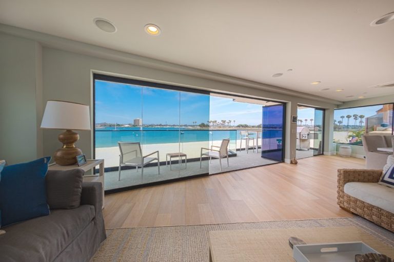 Looking from living and dining room out to patio with an opening in enclosed frameless sliding glass doors.