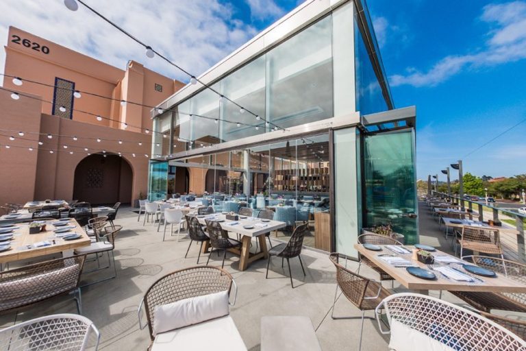 Restaurant patio dining area with opened frameless sliding glass doors.