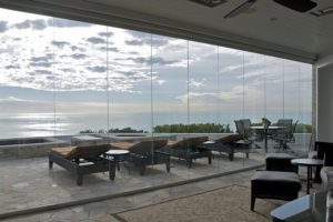 Closed frameless sliding glass doors connecting living area to outdoor patio with view of the ocean.
