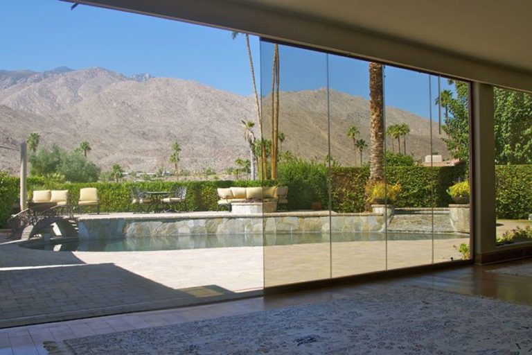 Living room with view of pool from half enclosed, half stacked frameless sliding glass doors.