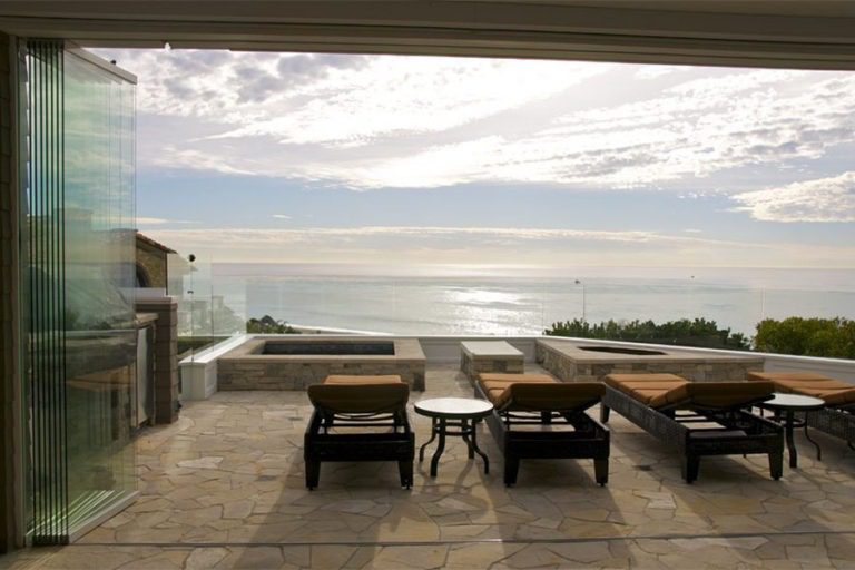 Outdoor patio with chaise lounge chairs and stacked sliding glass doors overlooking the ocean.