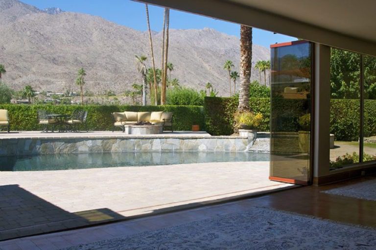 Living room with view of pool from stacked frameless sliding glass doors.