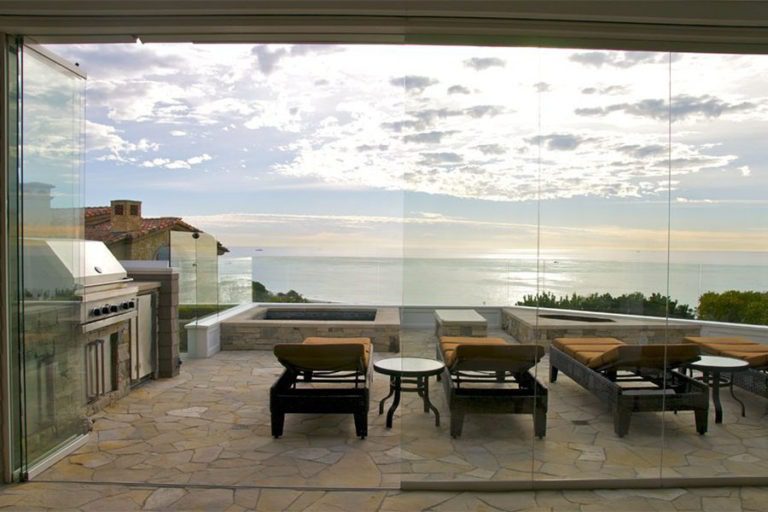 Outdoor patio with chaise lounge chairs and half open sliding glass doors overlooking the ocean.