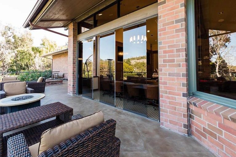 Outdoor patio looking into country club with partially open frameless sliding glass doors.