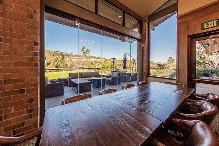 Country club with wood tables and leather chairs overlooking the patio and the yard through frameless sliding glass doors.