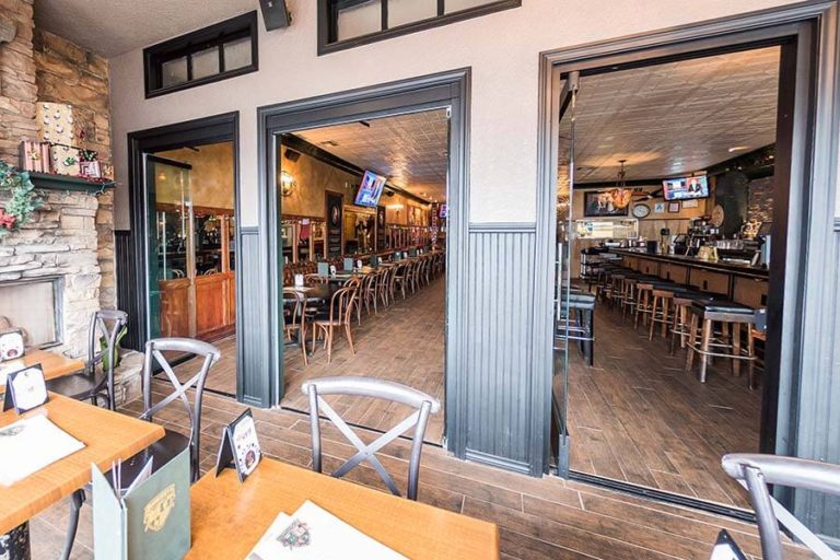 Outdoor restaurant tables looking inside the restaurant through three open frameless glass doors.