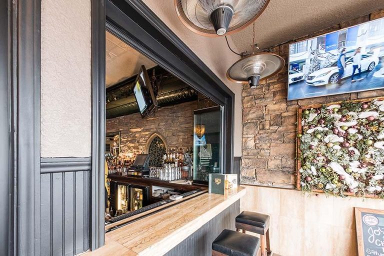 Fully stacked frameless glass window separating bar counter from the outdoor dining area.