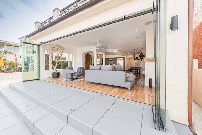 View of an open concept living room from outdoor area through fully stacked sliding glass doors.