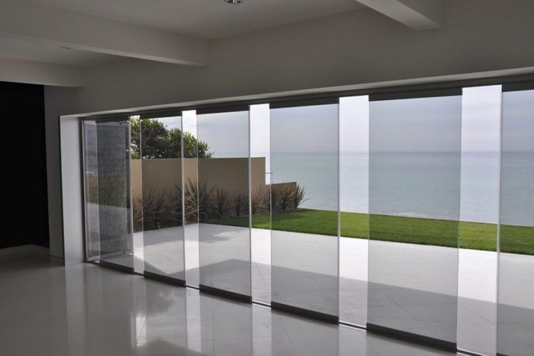 Empty room with partially open frameless sliding glass doors overlooking the ocean.