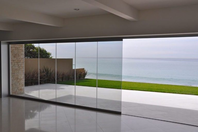 Empty room with half open frameless sliding glass doors overlooking the ocean.