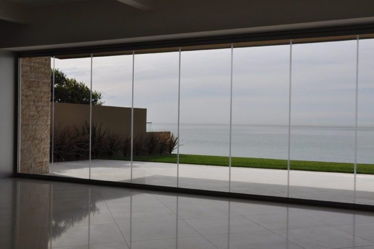 Empty room with fully closed frameless sliding glass doors overlooking the ocean.