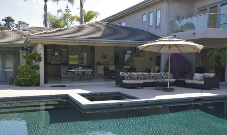 Pool with patio and stacked frameless sliding glass doors looking into kitchen and living room.