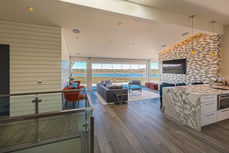 Living room and kitchen with enclosed frameless glass sliding doors and view of estuary.