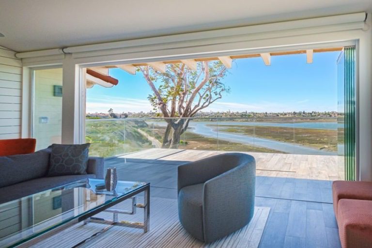 Living room with stacked frameless sliding glass doors and view of patio and estuary.