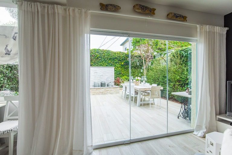 Enclosed frameless sliding glass doors with unobstructed views of backyard with fountain and table.