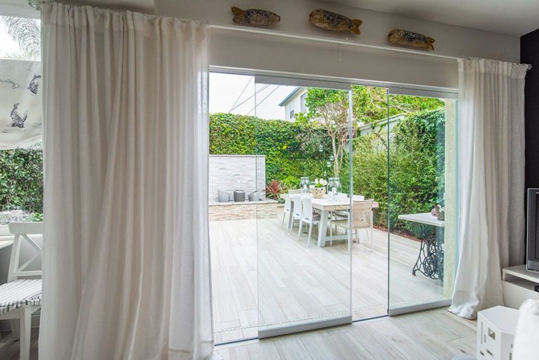 Staggered frameless sliding glass doors with an unobstructed view of the backyard with a fountain and table.