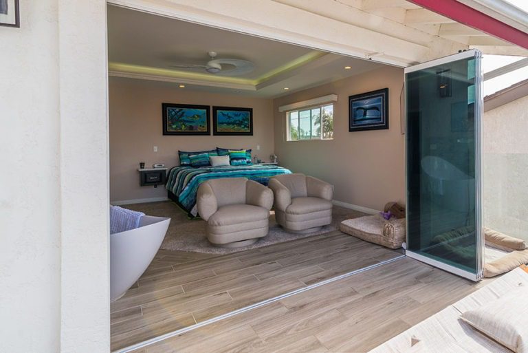 Looking into bedroom with wood flooring with frameless sliding glass doors stacked to the right of the doorframe from patio.