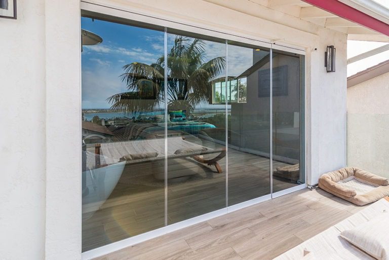 Looking from wooden floor patio at enclosed frameless sliding glass doors to the bedroom.