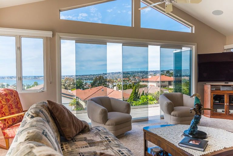 Looking from the living room to the patio with frameless sliding glass doors staggered with one door frame swung open in doorframe of the patio allowing for unobstructed views of the bay.