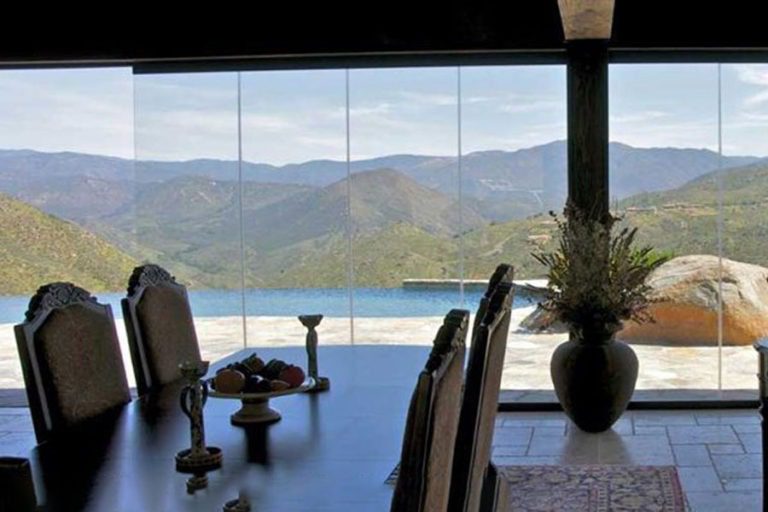 Dining area overlooking the outdoor patio with swimming pool and mountains in the back through frameless sliding glass doors.