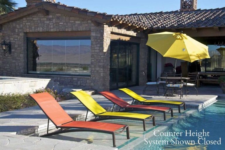 Swimming pool with poolside chairs and residence on the back featuring closed counter height glass panels.