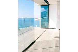 Half enclosed, half- stacked frameless sliding glass doors with patio and ocean view.
