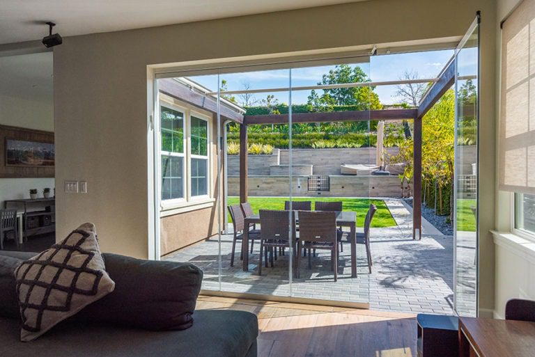 Looking from living room into backyard with enclosed frameless sliding glass doors and and opened door.