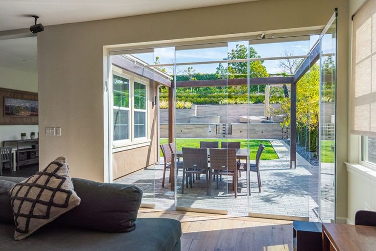 Looking into living room into backyard with staggered frameless sliding glass doors.