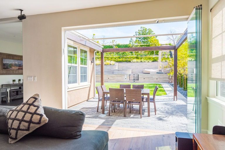 Looking from living room into backyard with opened frameless sliding glass doors left to one side of room.