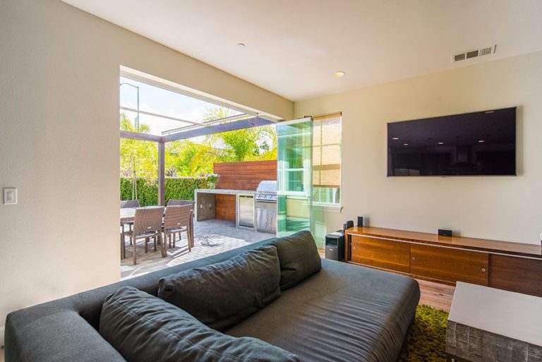 Looking from living room into backyard with patio with opened frameless sliding glass doors left to one side of room.