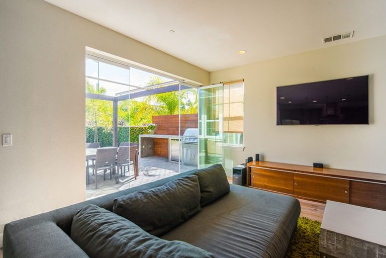 Looking from living room into backyard with patio with staggered frameless sliding glass doors and door swung open.