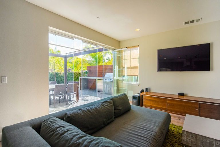 Looking from living room into backyard with patio and barbecue with staggered frameless sliding glass doors and door swung open.