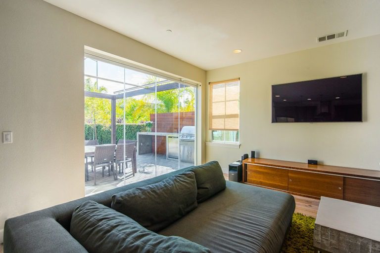 Looking from living room into backyard with patio and barbecue with enclosed frameless sliding glass doors.