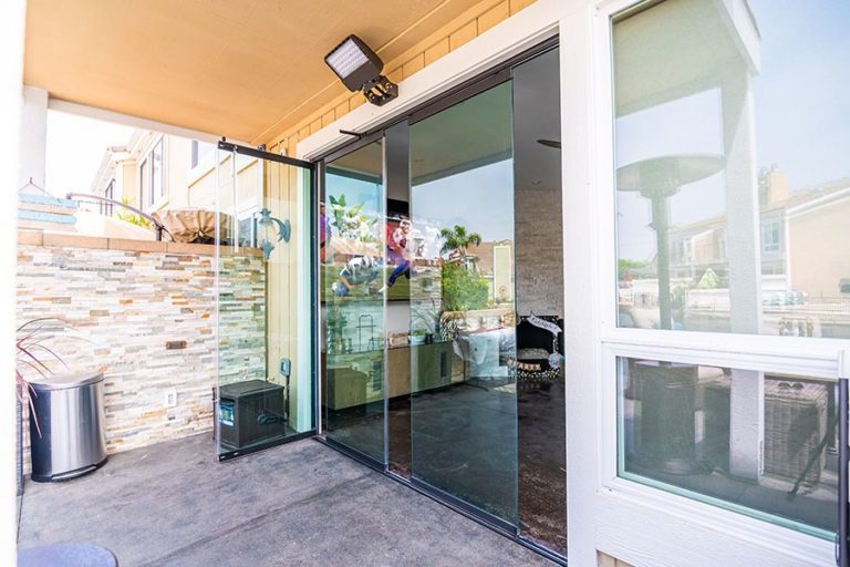 Outdoor area with partially closed frameless sliding glass doors looking into living room.