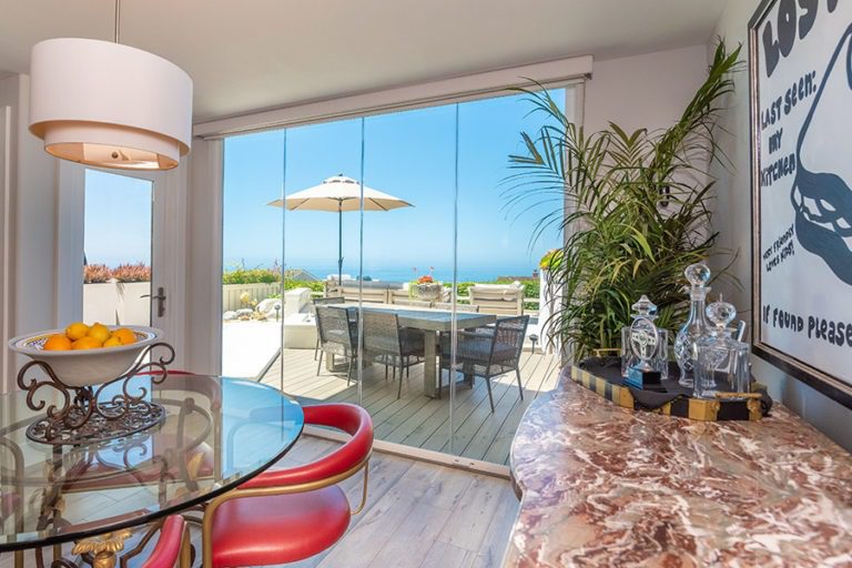 Dining room with enclosed frameless glass doors and unobstructed views of the ocean and table on patio.